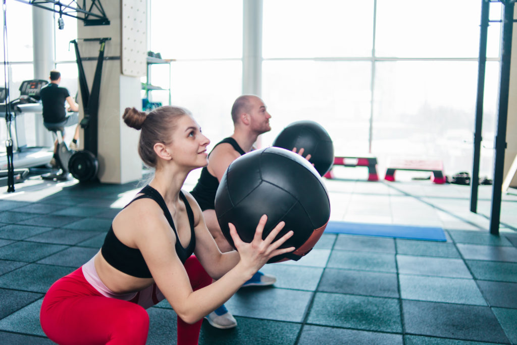 Man and woman doing a squat movement with a medicine ball as part of their all access membership
