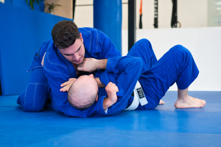 Two men training brazilian jiu jitsu on the mats during open mat positional training while taking classes throughout the day